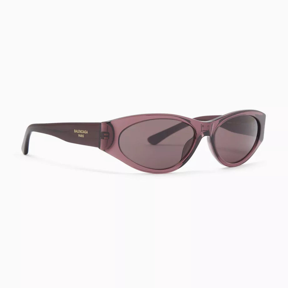 A pair of cat-eye sunglasses with a translucent dusty rose frame and dark tinted lenses, shown on a clean white background. The brand name 'BURGA' is visible in gold lettering on the temple arm.