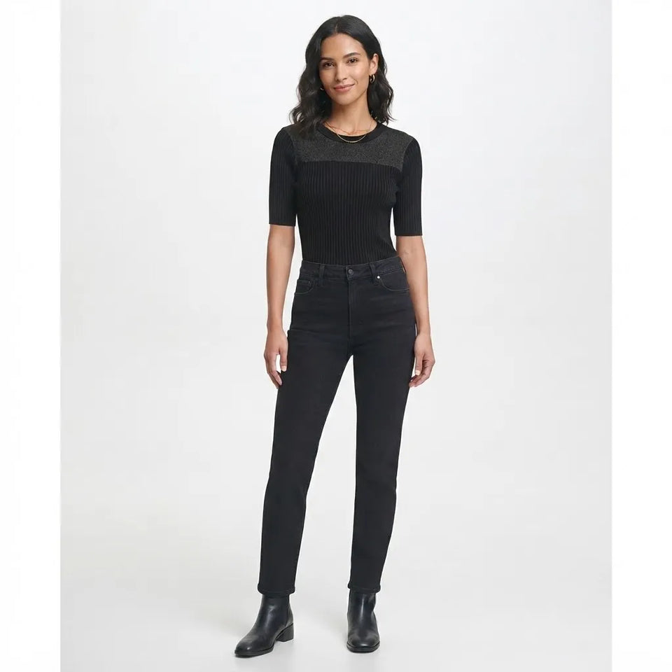 A woman modeling a black short-sleeve ribbed knit top with a sheer textured yoke and black skinny jeans against a light gray studio background.