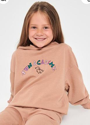 Child wearing a beige hoodie with 'FUN ACADEMY' text and dog graphic on a white background