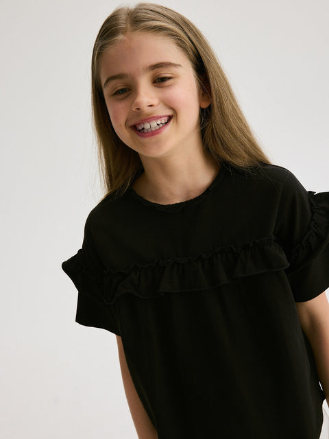 Young girl wearing a black top with ruffled details on a plain background