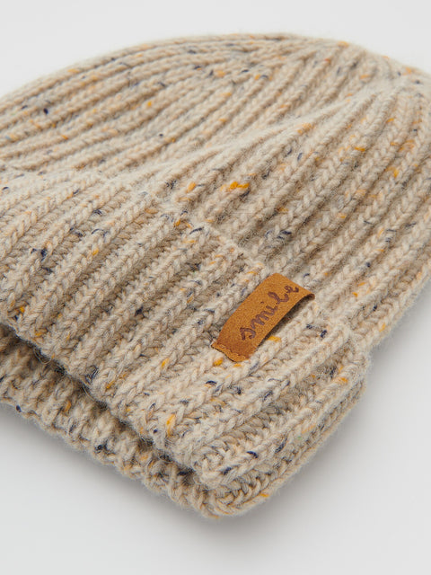 Beige knitted beanie with a brand label on a light gray background