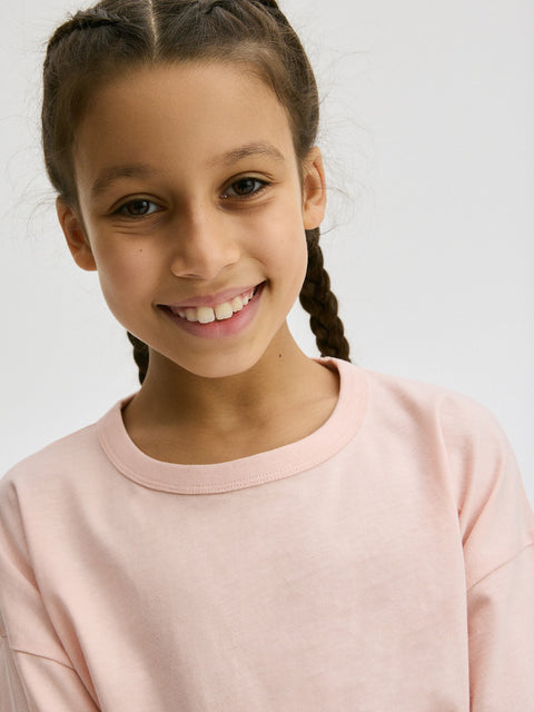 Young girl wearing a light pink sweatshirt against a plain background