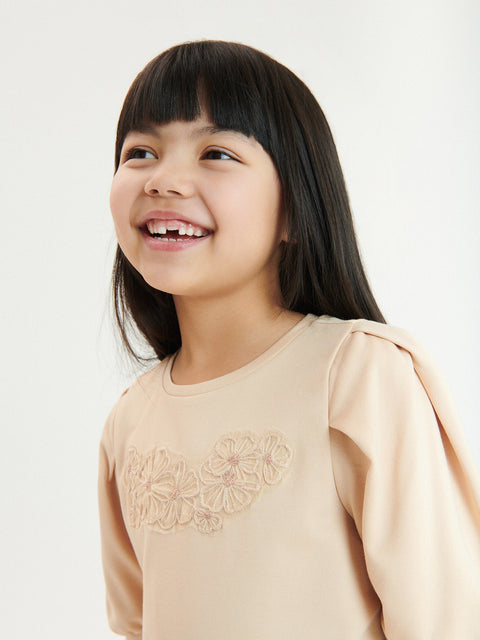 Young girl wearing a beige top with floral embroidery on a white background