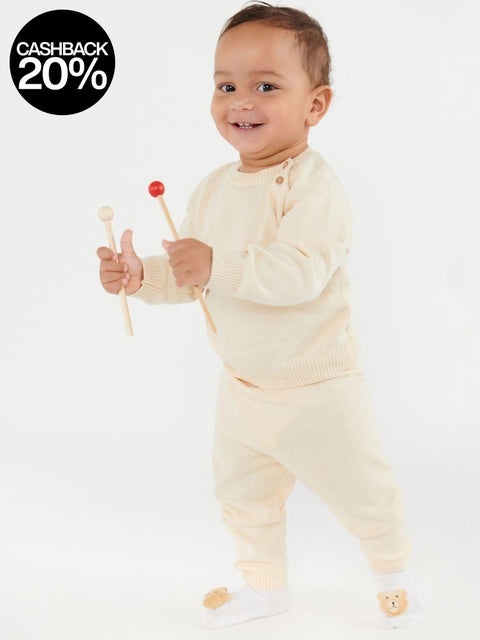 Baby in a cream outfit holding wooden toys on a white background