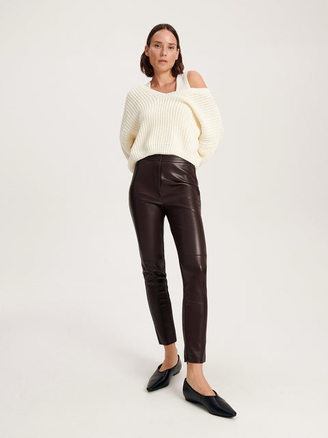 Woman wearing a white sweater and black leather pants on a white background