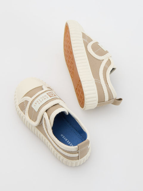 Pair of beige slip-on sneakers with a blue sole on a light gray background