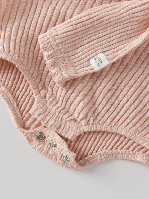 Close-up of a pink ribbed baby romper with a brand label on a light gray background