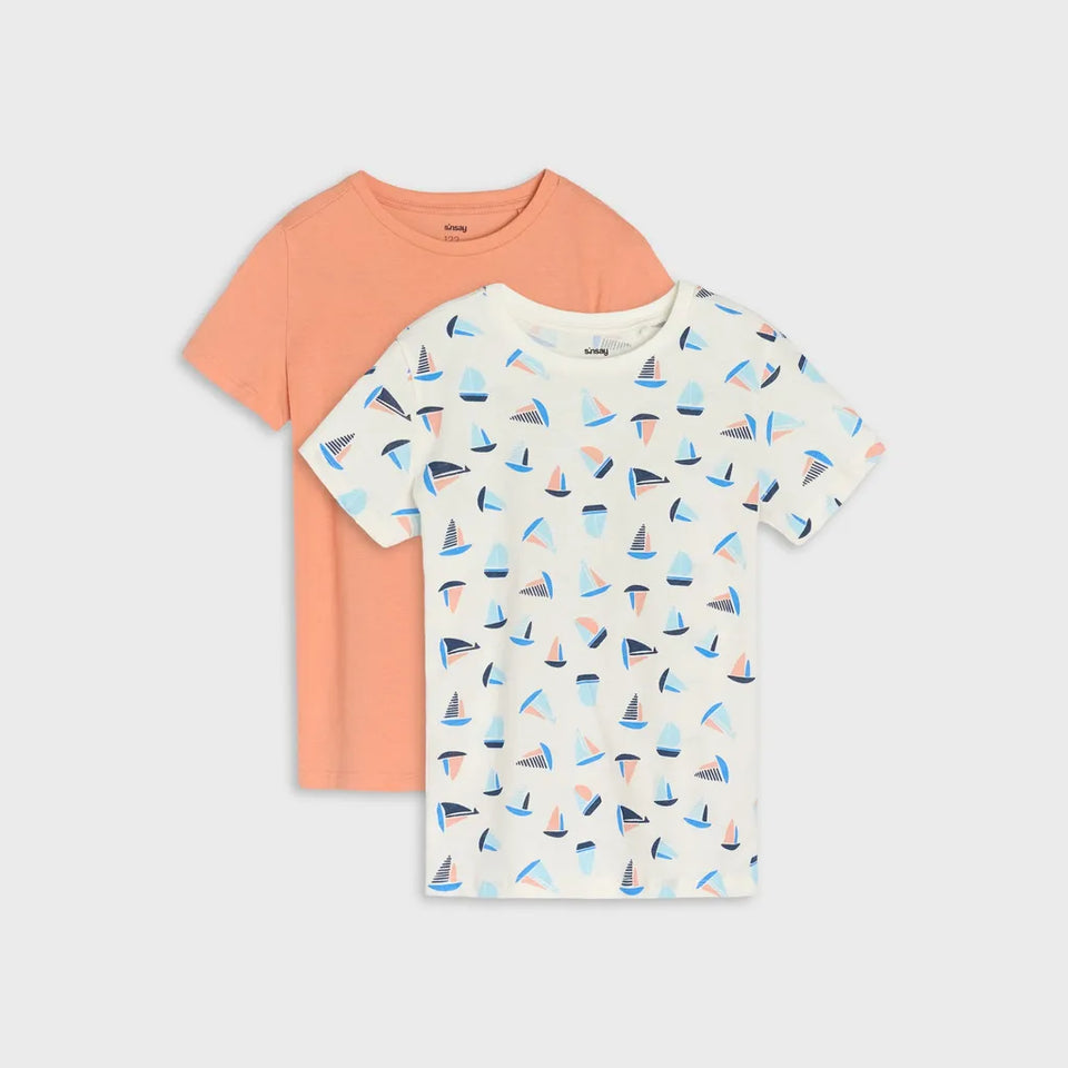 Two short-sleeve kids' t-shirts by VOGUE on a light gray background. The front shirt is off-white with a repeating sailboat print in blue, orange, and gray.