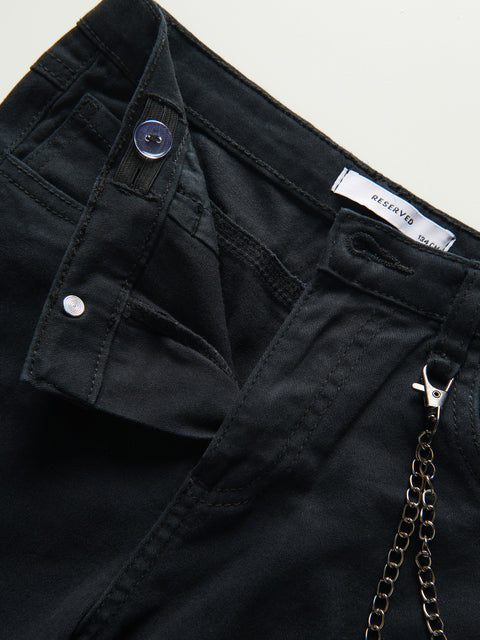 Close-up of black pants with a chain detail and button on a light gray background
