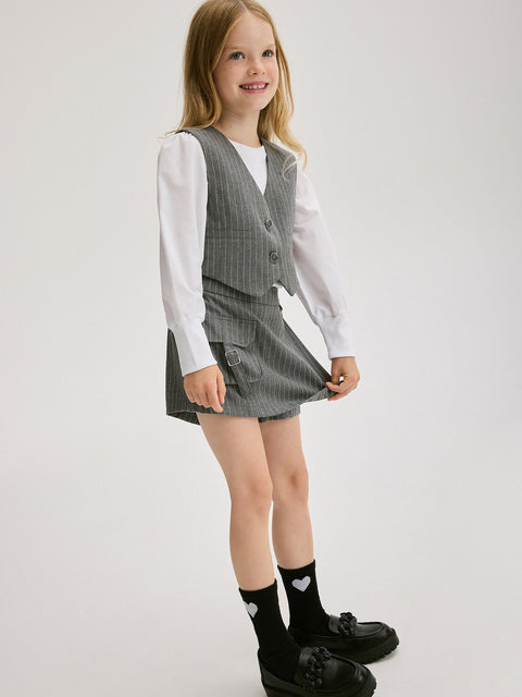 Young girl wearing a gray checkered vest and skirt set on a white background