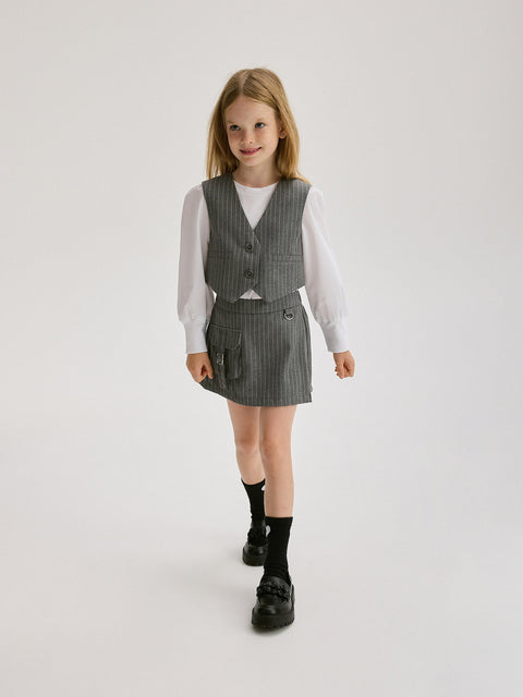 Young girl wearing a gray checkered vest and skirt set on a white background
