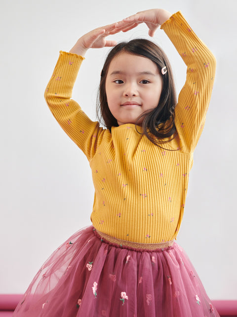 Young girl wearing a yellow top and pink skirt with a white background