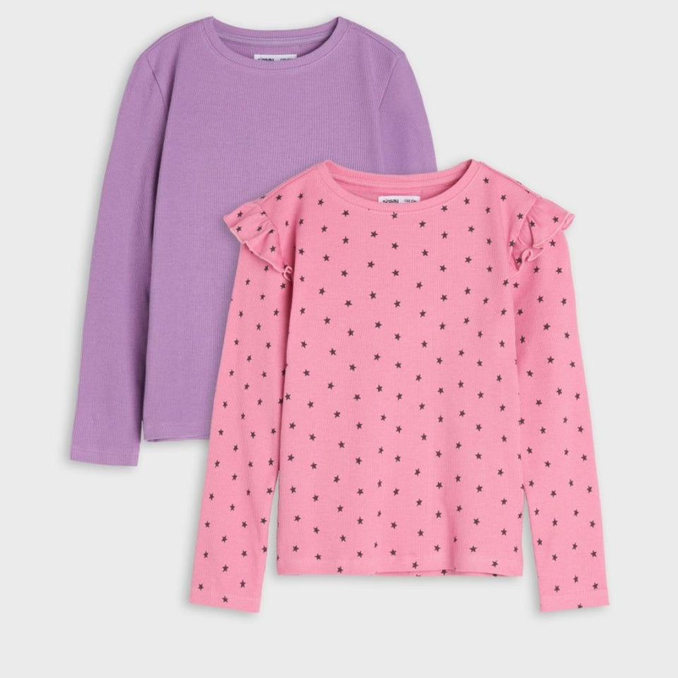 Two girls' long-sleeve tops on a light gray background: one solid lavender purple and one pink with small black polka dots and ruffled shoulder details.