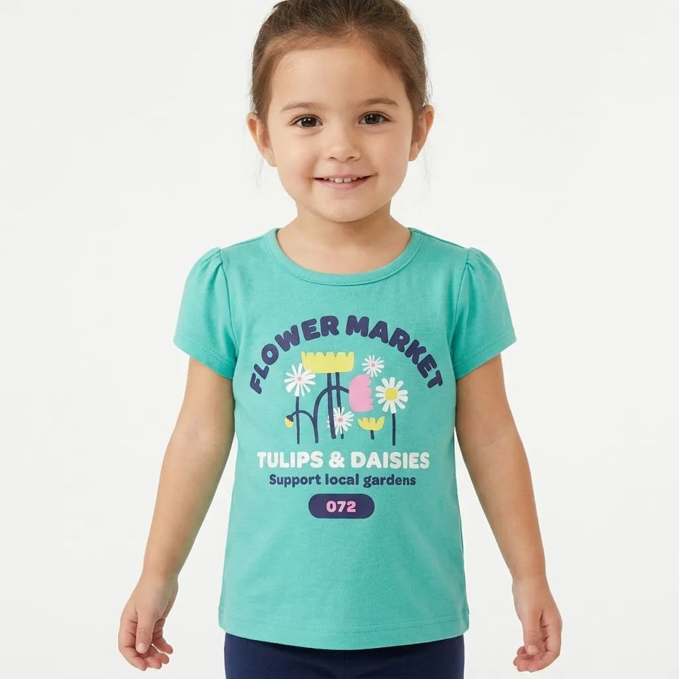 A young girl wearing a turquoise short-sleeve t-shirt with a colorful 'Flower Market' graphic on the front, paired with dark blue pants, standing against a light gray studio background.