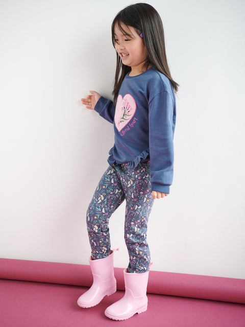 Child wearing a blue sweatshirt with a heart design, patterned pants, and pink boots on a white background.