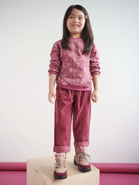 Young girl wearing a pink patterned sweater and corduroy pants on a white background