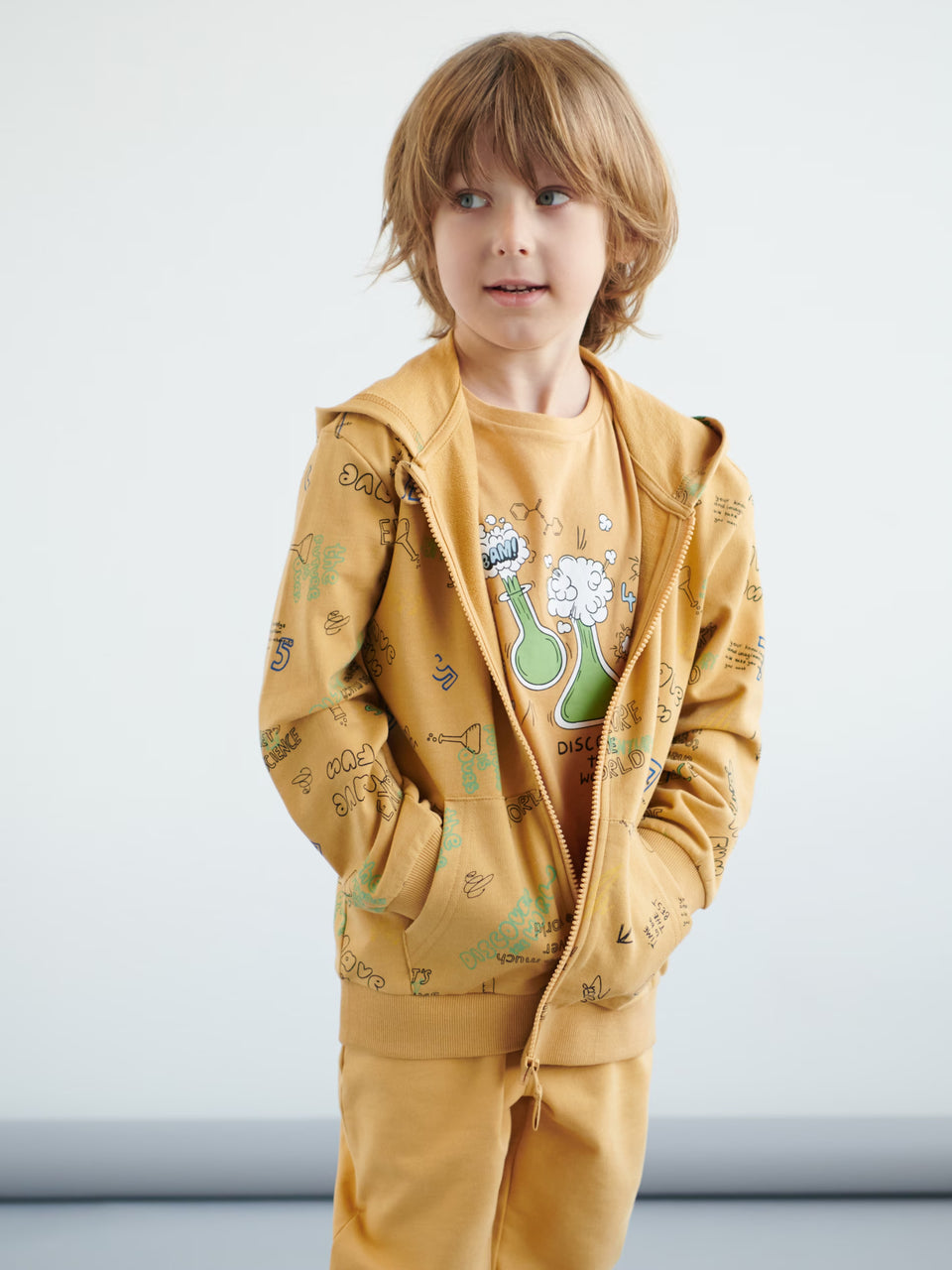 Child wearing a mustard yellow hoodie and pants with a graphic design on a white background