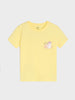 A pale yellow short-sleeve crewneck t-shirt featuring a small cartoon unicorn graphic on the left chest, displayed against a light gray background.