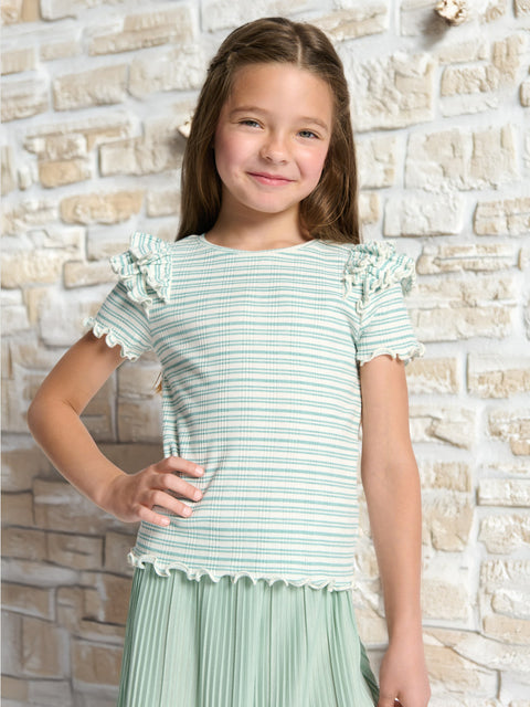 Young girl wearing a green and white striped shirt with ruffled sleeves against a stone wall.