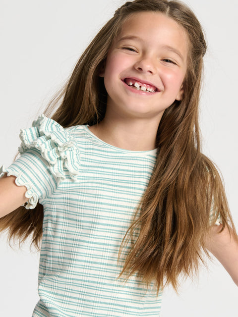 Young girl wearing a green and white striped shirt with ruffled sleeves on a plain background