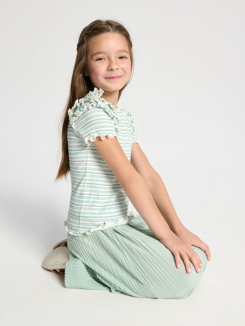 Young girl wearing a green and white striped outfit sitting on a white background