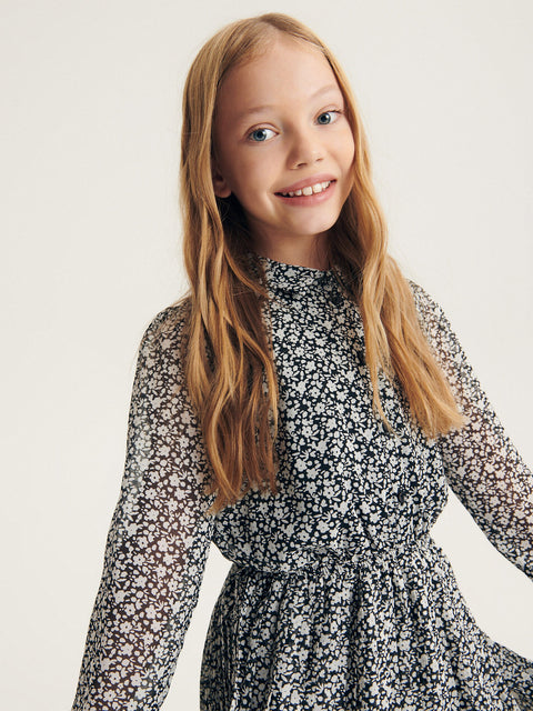 Young girl wearing a black floral dress against a plain background