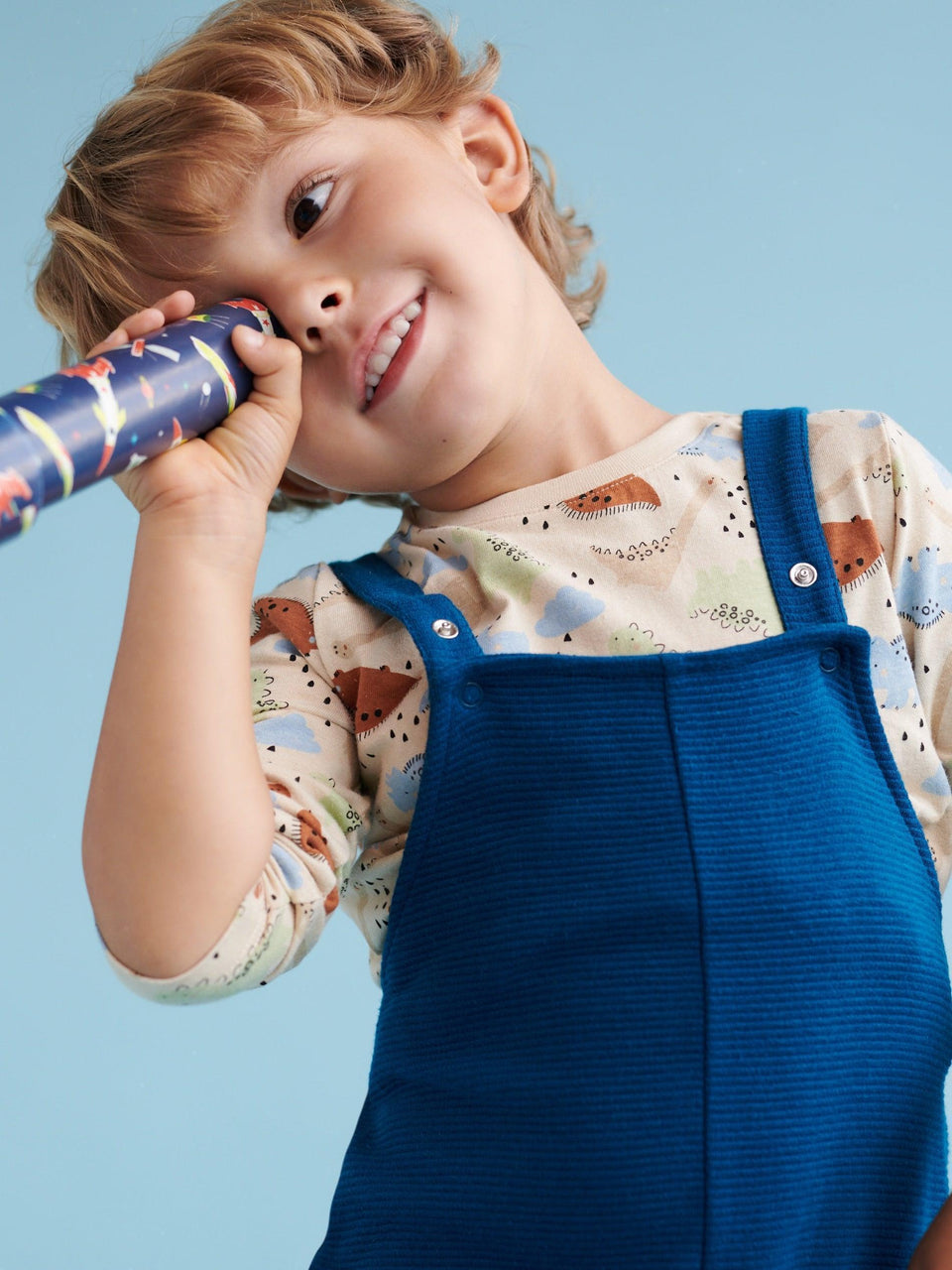 Child wearing a blue dress overalls holding a toy against a light blue background with a cashback offer overlay.