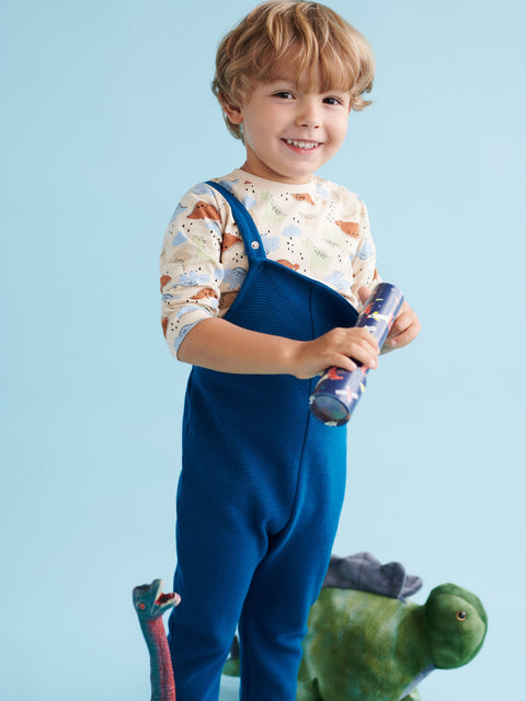 Child wearing blue overalls holding a toy against a light blue background