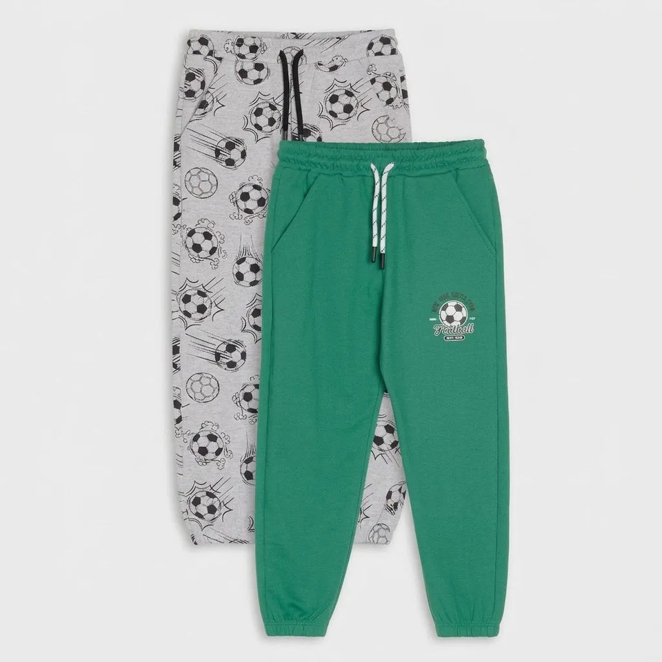 Two pairs of kids' sweatpants displayed flat against a light gray background. The front pair is bright green with a small soccer-themed crest on the left thigh and white drawstrings.