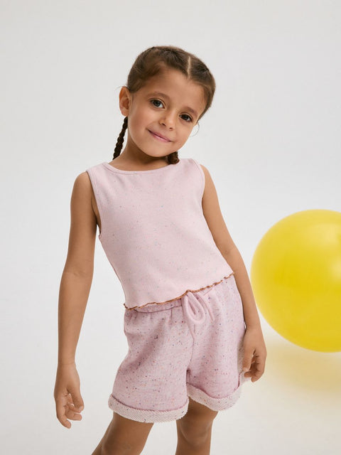Young girl in a pink outfit standing next to a yellow ball on a light gray background