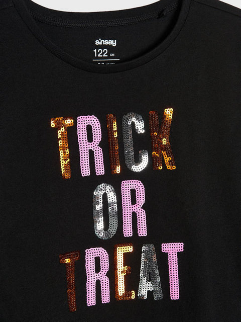 Black t-shirt with 'Trick or Treat' text in colorful sequins on a plain background