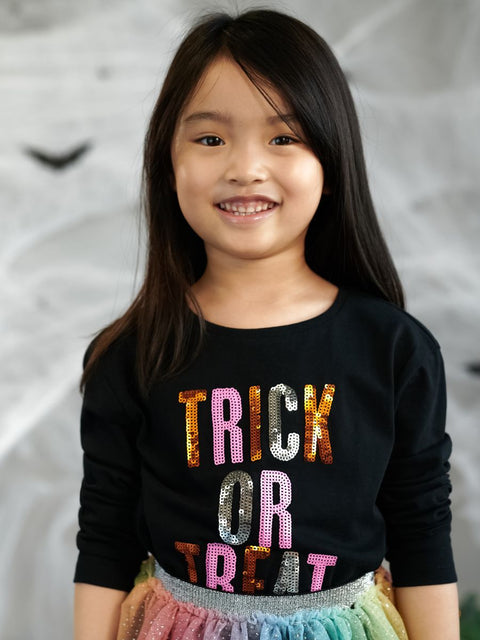 Young girl wearing a black shirt with 'TRICK OR TREAT' in colorful letters against a neutral background