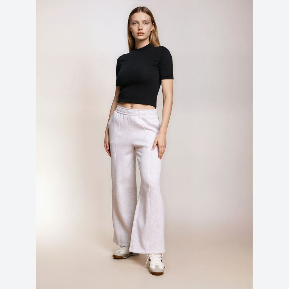 A woman modeling a black short-sleeve crop top and light heather gray wide-leg sweatpants against a plain beige studio background.