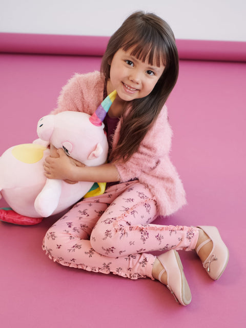 Child holding a unicorn plush toy on a pink floor