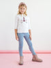 Young girl wearing a white shirt with a unicorn design, blue jeans, and pink boots on a white background.