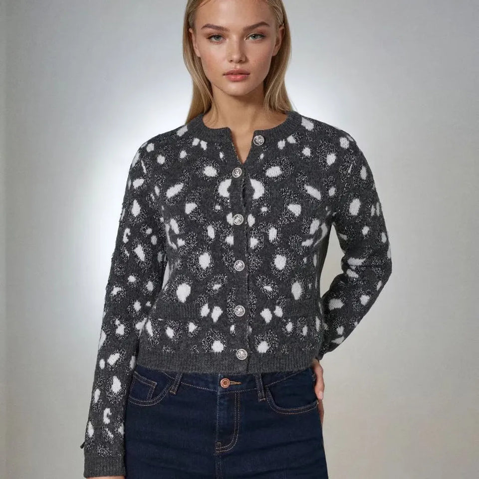 A woman modeling a dark gray knit cardigan with a white spotted pattern, paired with dark blue jeans, against a neutral gray studio background.