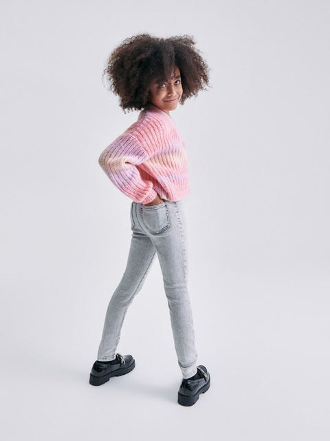 Person wearing a colorful sweater and gray jeans on a white background