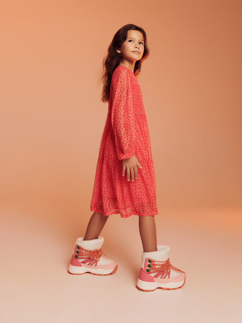Young girl wearing a red dress and pink boots against a peach background