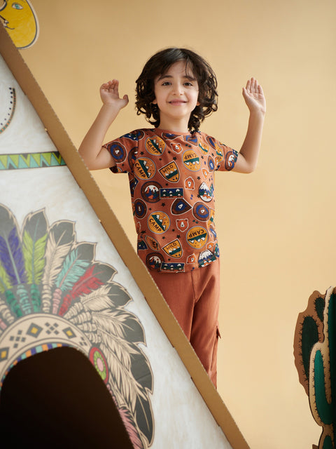 Child wearing a patterned shirt and brown pants standing in front of a colorful wall with geometric shapes.