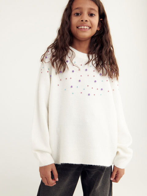Child wearing a white sweater with colorful dots on a plain background