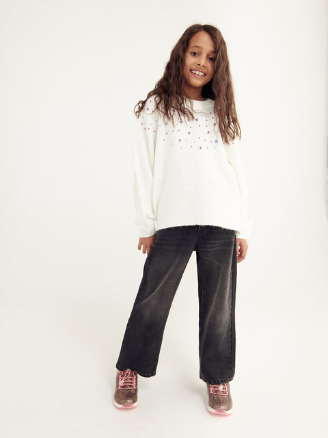Young girl wearing a white sweater with star patterns and dark jeans on a white background