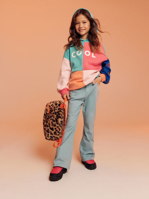 Child wearing a colorful hoodie and holding a leopard print bag on a beige background