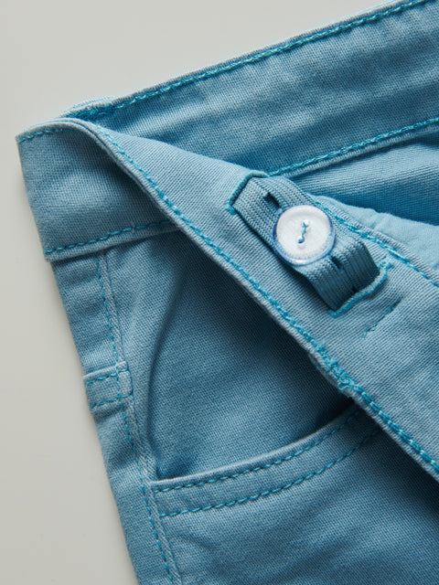 Close-up of a blue denim pocket with a button on a light gray background