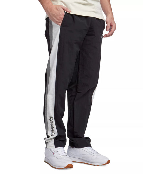 Person wearing black track pants with a white stripe and white sneakers on a white background