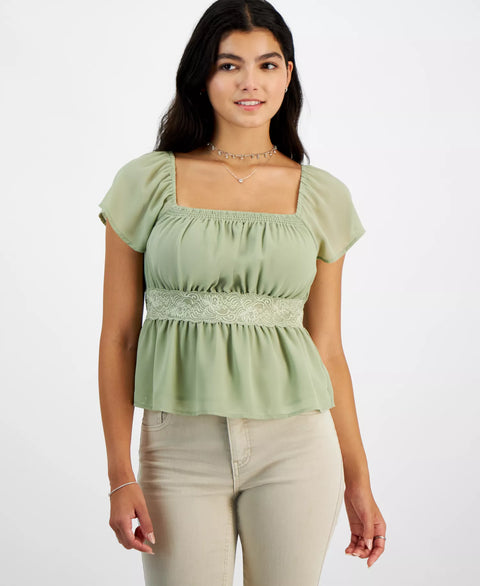 Woman wearing a light green top with lace detail on a white background