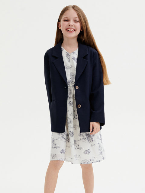 Young girl wearing a navy blazer over a floral dress on a white background