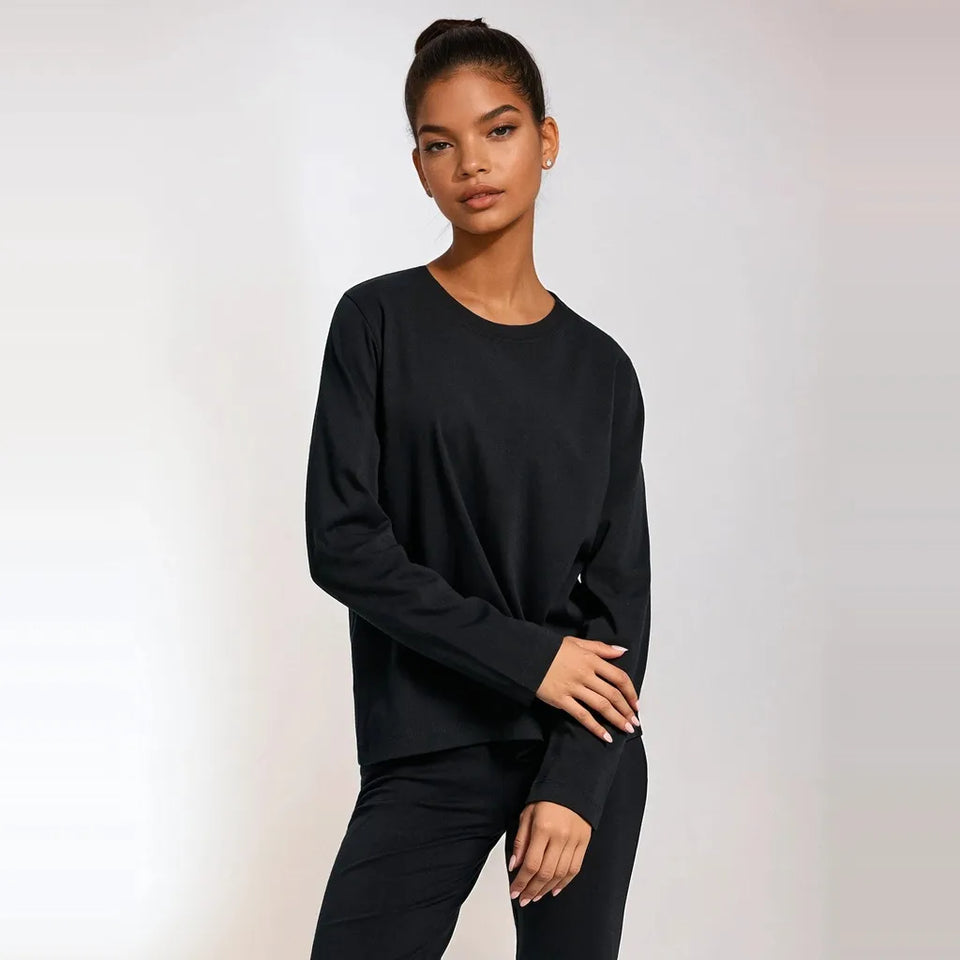 A woman modeling a black long-sleeve crewneck top and matching black pants against a light gray studio background.