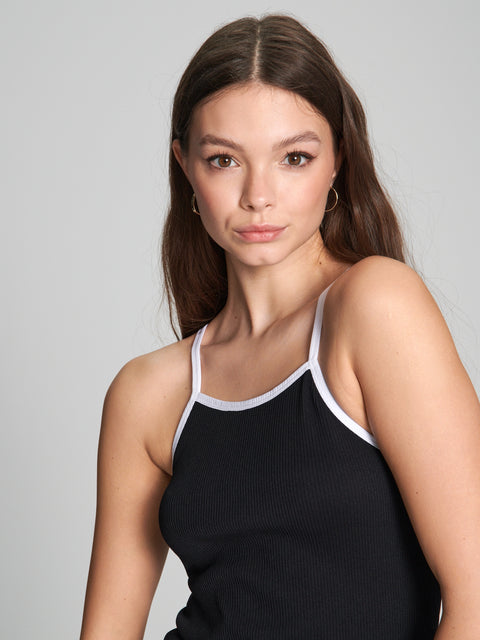 Woman wearing a black tank top with white straps against a gray background