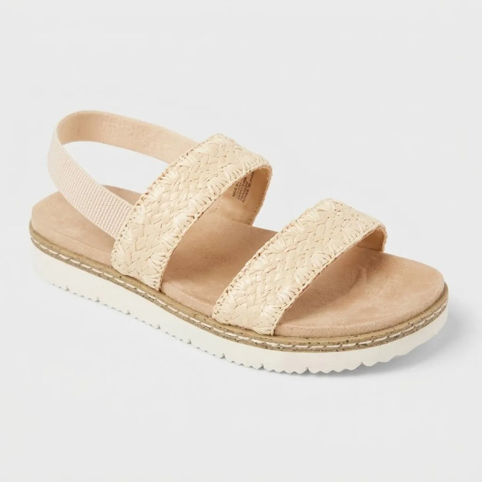 A single women's espadrille-style sandal in a light beige/tan color, featuring woven straps, a fabric ankle strap, and a white wavy sole, shown on a light gray background.