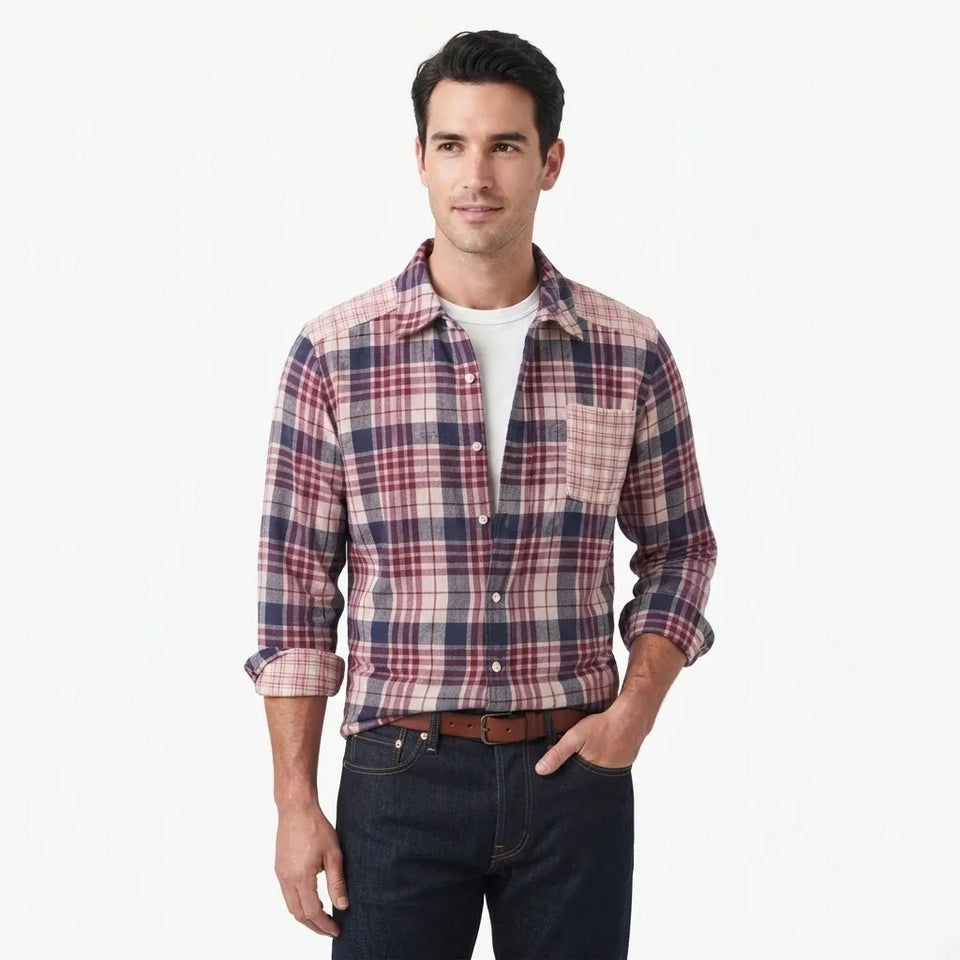 A man wearing a long-sleeve button-up plaid flannel shirt in red, navy, and beige, paired with a white t-shirt, dark blue jeans, and a brown leather belt, photographed against a solid white background.